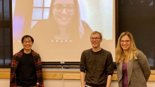 three graduate students in front of projector screen