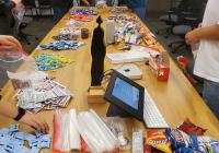 Large conference table covered with snacks, supplies. Students stand around the table putting items in bags.