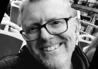 black and white photo of Derek Kreager, wearing glasses and smiling into the camera